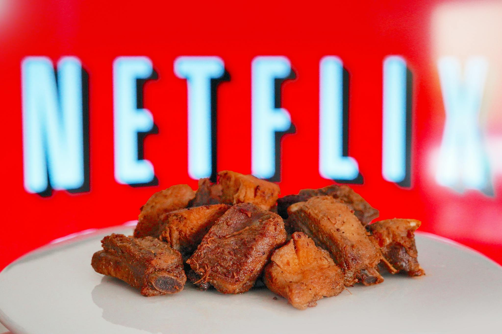 Plate of roasted beef ribs in front of a bright Netflix screen, perfect for a cozy night in.